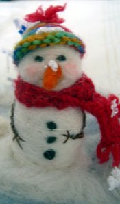 needlefelted snow person wearing a handknitted cap and scarf